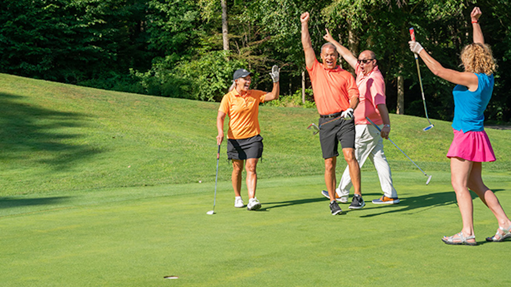 Four friends cheering with excitement after a putt goes in on the Double Black Diamond Golf Course.